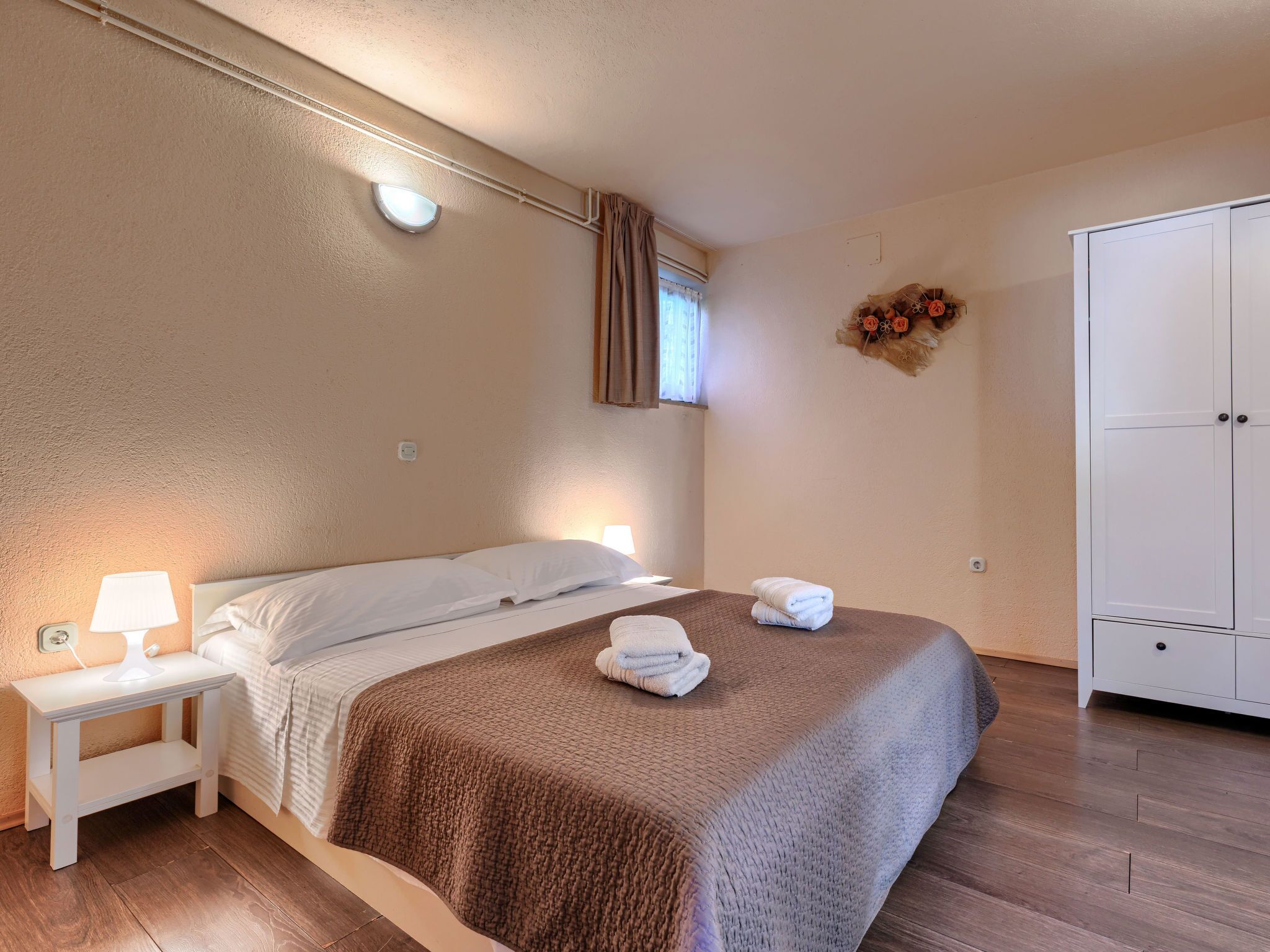 A bedroom with a bed, a nightstand, a wardrobe, and a wall-mounted light fixture.