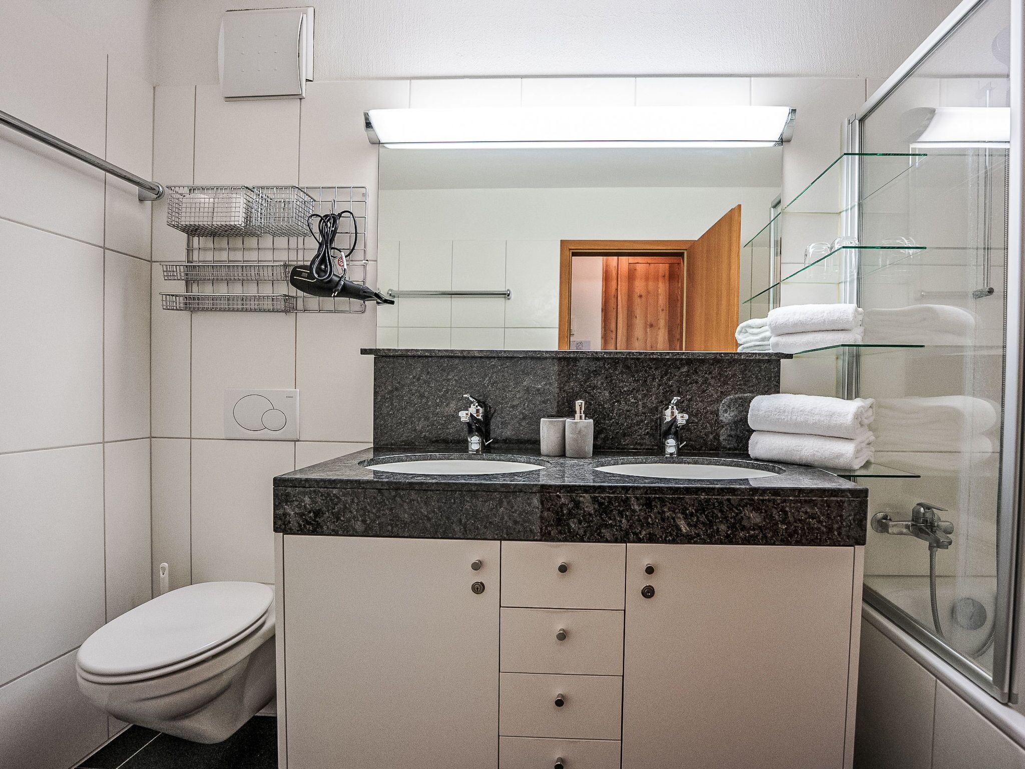 A modern bathroom with a double sink vanity, a glass shower enclosure, and a toilet.