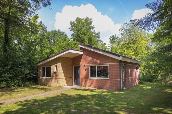 Une maison de plain-pied en briques, avec un toit en pente, une porte d’entrée et un petit porche.