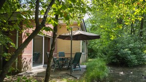 A patio with a table and chairs, a brick building, and a pond with ducks. - 6-Person Comfort holiday home with Sauna. (Kootwijk)
