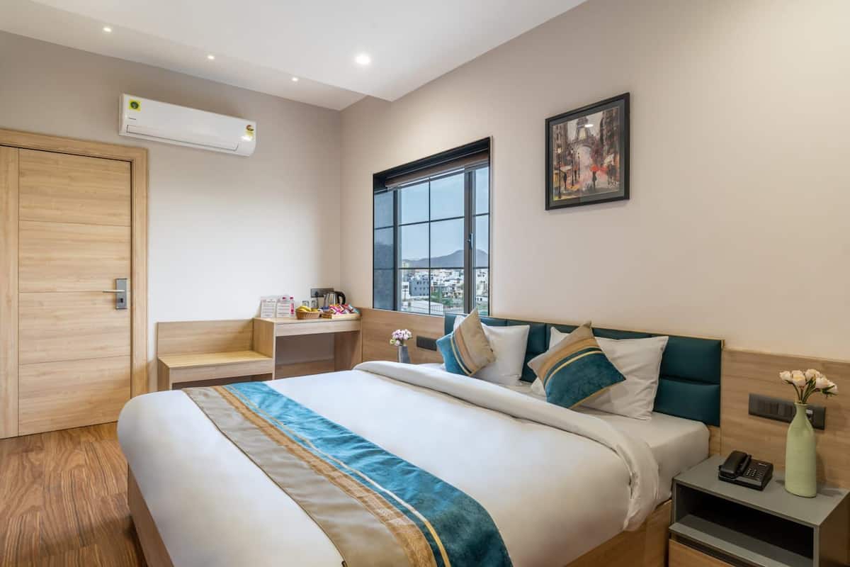 Una habitación de hotel moderna con una cama grande, un escritorio, una ventana con vistas a la ciudad, un equipo de aire acondicionado y un cuadro en la pared.