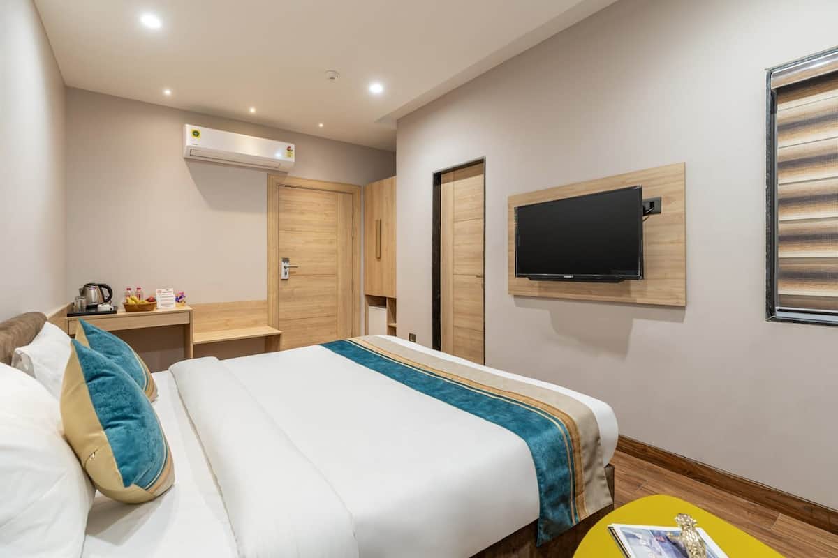 Habitación de hotel con cama, televisor montado en la pared, armario de madera y una mesita con tetera y tazas.