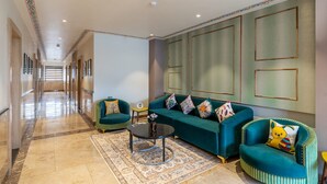 A spacious lobby with a long corridor, a teal sofa set, a patterned rug, and a small table with a vase. - The Hoften DiVi Hotel Aradhya Inn (Udaipur)