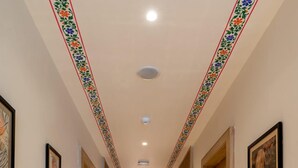 A long, well-lit hallway with marble floors and doors on both sides, leading to a staircase at the end. - The Hoften DiVi Hotel Aradhya Inn (Udaipur)