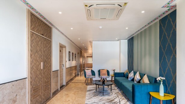 A hotel lobby with a herringbone-patterned wall, a blue sofa set, a patterned rug, and a ceiling air conditioner. - The Hoften DiVi Hotel Aradhya Inn (Udaipur)