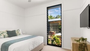 Un dormitorio con cama, una mesita de noche con una planta, una puerta corrediza a un balcón y un televisor montado en la pared.