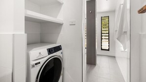 Un moderno lavadero con lavadora de carga frontal, una ventana pequeña con persianas y suelo de baldosas.