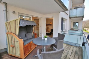 En balkon med fletningsmøbler, et rundt bord og gelænder af glas.