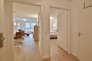 A modern interior with a wooden floor, a dining area with chairs and a table, and a bedroom with a bed and nightstand. - Strandglück Apartment 03A "Beachfront" - Strandglück House A (Scharbeutz)