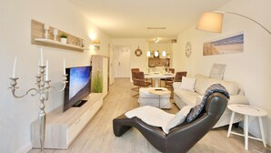 Ett modernt vardagsrum med en platt-TV, en läderfåtölj, en matplats med ett runt bord och ett kök i bakgrunden.
