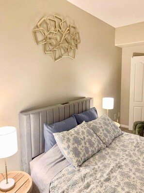 Une chambre à coucher comprenant un lit, une tête de lit, un luminaire fixé au mur et une porte.