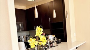 Una cucina moderna con mobili scuri, elettrodomestici in acciaio inossidabile, un piano di lavoro bianco e lampade a sospensione.