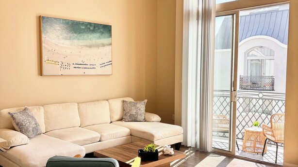 Un soggiorno con un divano color beige, un tavolino da caffè con una pianta e vista su un balcone con mobili da esterno.