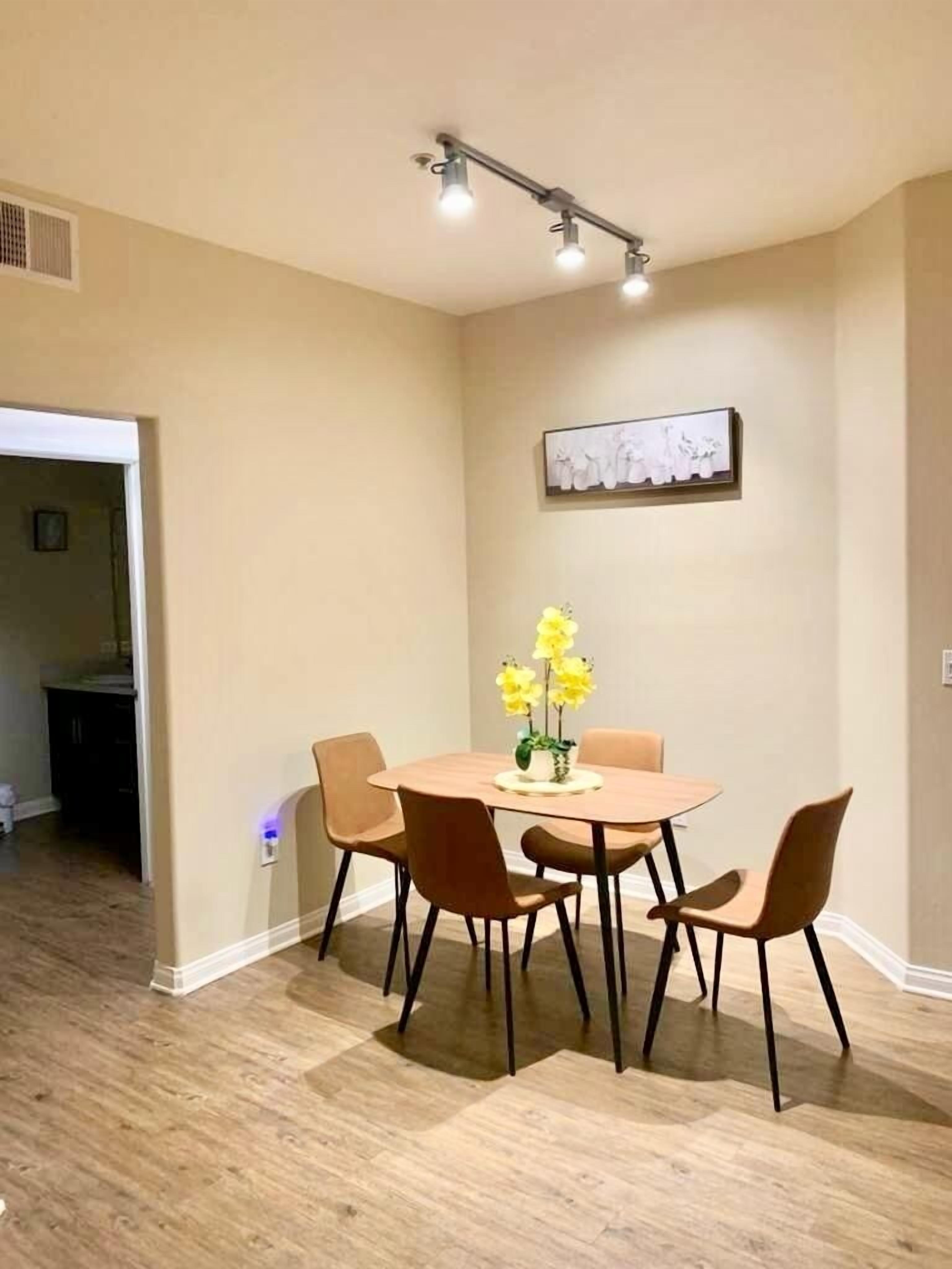 Un coin repas avec une table ronde, quatre chaises et un vase rempli de fleurs jaunes.