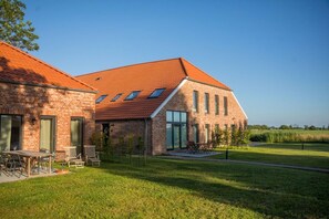 A modern brick building with a sloped red-tiled roof, large windows, and a grassy lawn. - Gulfhof Wangermeer 2: A self-contained Tilda unit with a terrace and modern amenities - (Wangerland)