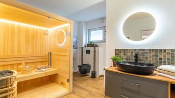 Ein modernes Badezimmer mit einer Holzsauna, einem schwarzen Beckenwaschbecken und einem großen Spiegel.