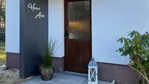 Ein modernes Gebäude mit dunkler Fassade, einer Holztür und einem Schild mit der Aufschrift 'Haus Alex'.