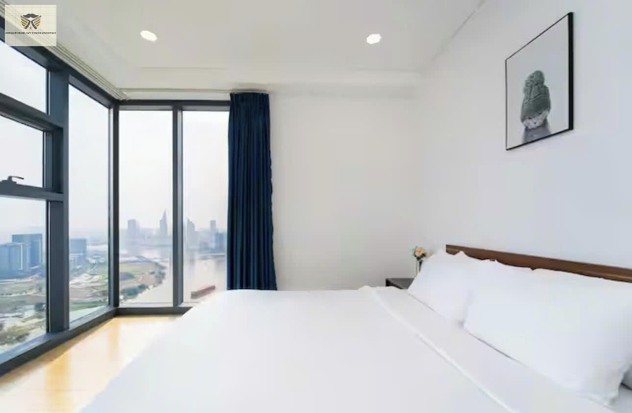 A hotel room with a large bed, a city view through floor-to-ceiling windows, and a framed artwork on the wall.