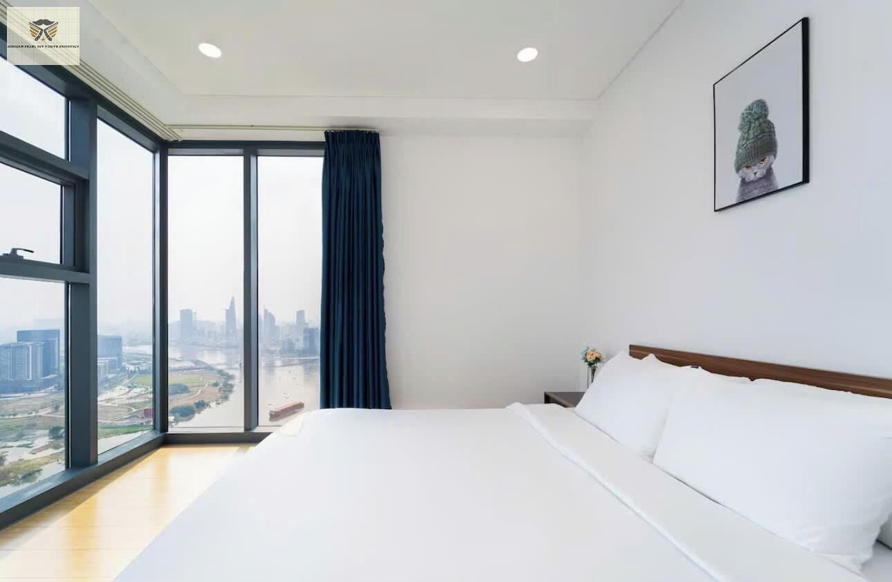 A modern hotel room with a large bed, a city view, and a framed picture on the wall.