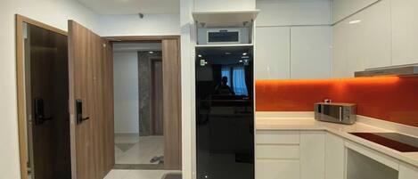 A modern kitchen with white cabinets, a microwave, and a sink. There is a wooden door and a view into another room.