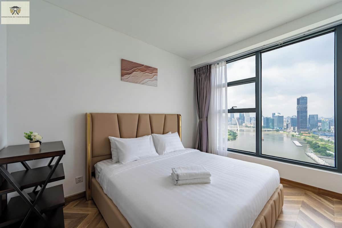 Une chambre d’hôtel avec un grand lit, un bureau et une vue sur le paysage urbain, visible à travers une grande fenêtre.