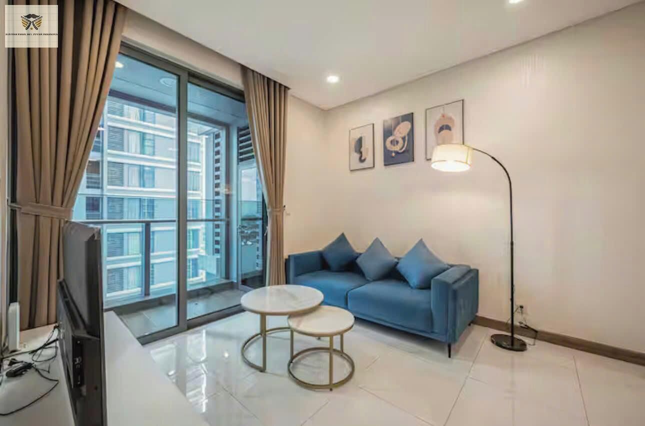 Un salon moderne avec un canapé bleu, deux petites tables rondes, un lampadaire et un téléviseur.
