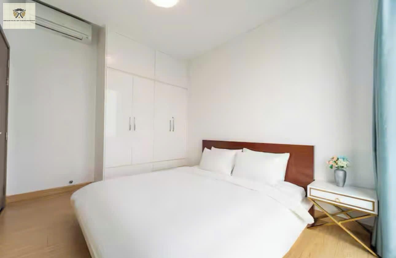 A hotel room with a large bed, a wooden headboard, a white nightstand, and a wardrobe with multiple doors.