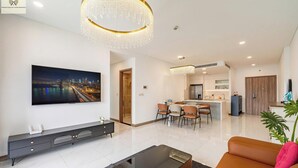 Ein modernes Wohnzimmer mit Flachbildfernseher, Essbereich mit Stühlen, Küche inklusive Kühlschrank und einer Kronleuchter.