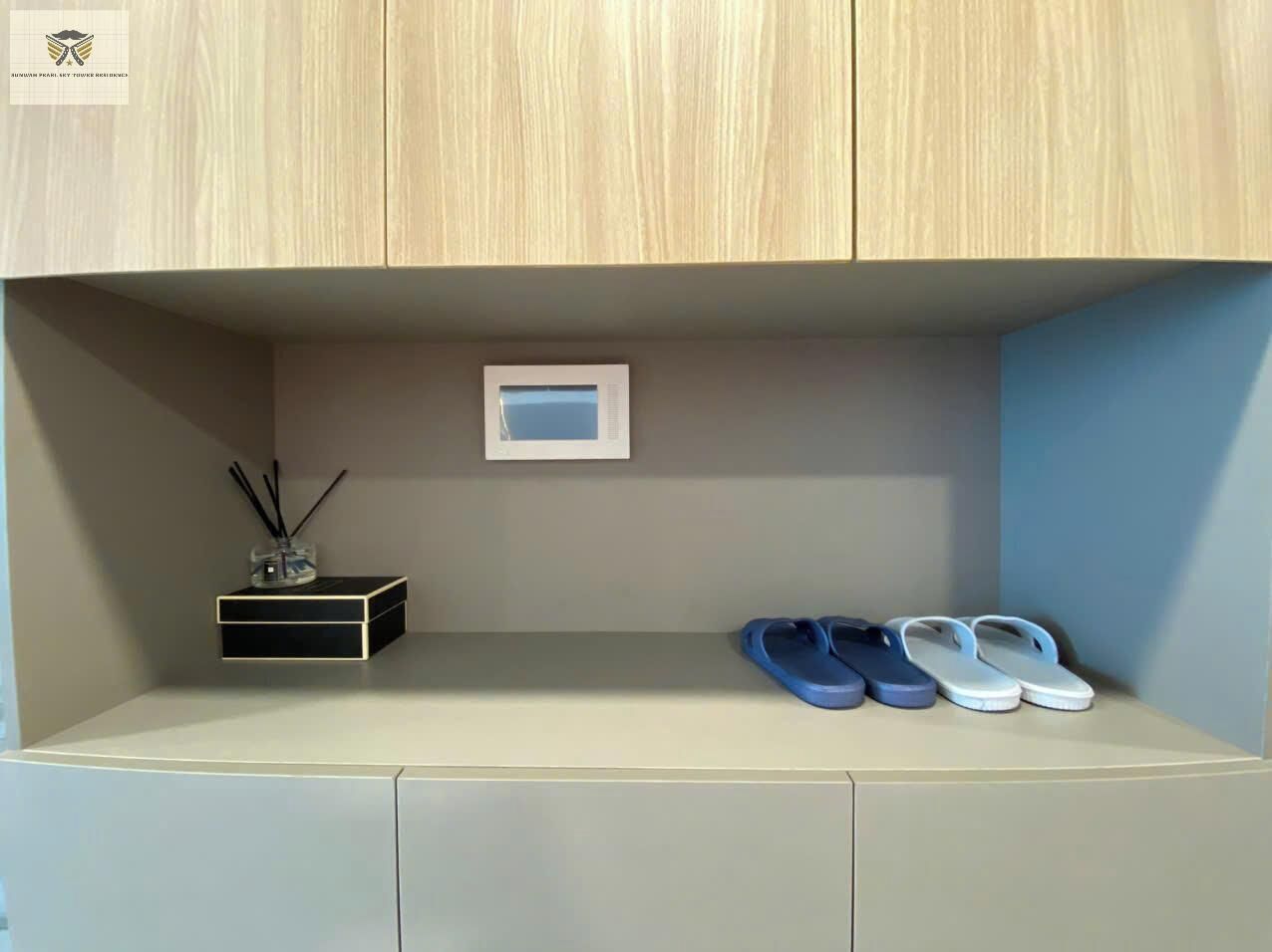 A wooden cabinet with a shelf containing a small box, a pair of blue slippers, and a white object.