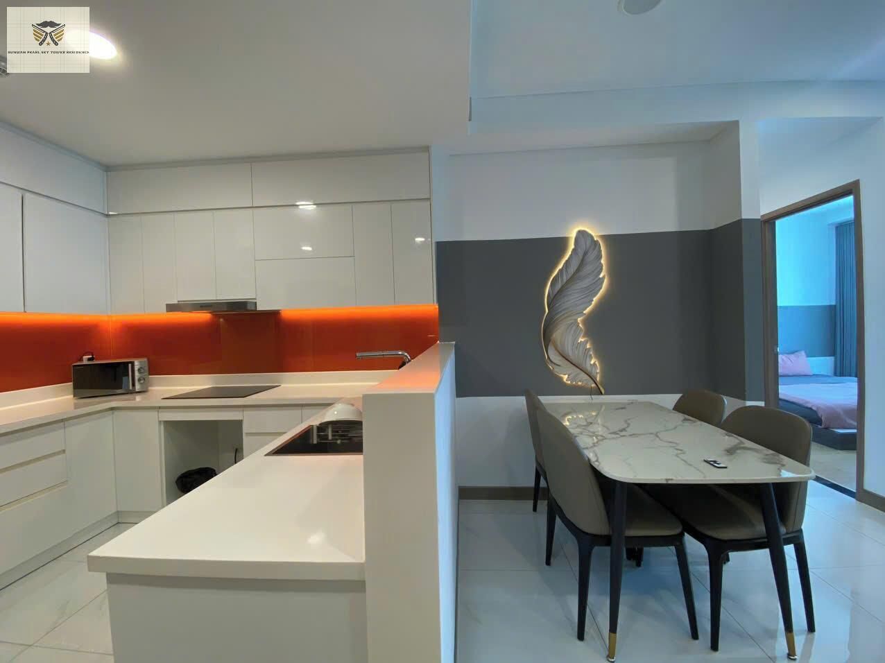 Uma cozinha moderna com armários brancos, uma parede de destaque laranja e uma sala de jantar com mesa e cadeiras de mármore.