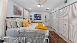 Un dormitorio con cama, ventilador de techo, un cuadro y armario.
