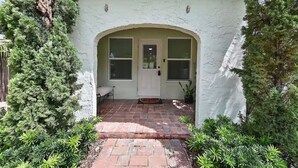 Una casa con entrada de ladrillo, una puerta blanca y un porche cubierto.