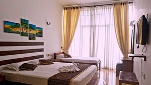 Habitación de hotel con dos camas, ventilador de techo, televisión y ventana con cortinas.