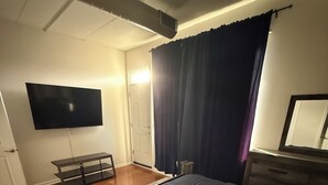 Un dormitorio con cama, televisor de pantalla plana montado en la pared, cómoda y ventana con cortinas.
