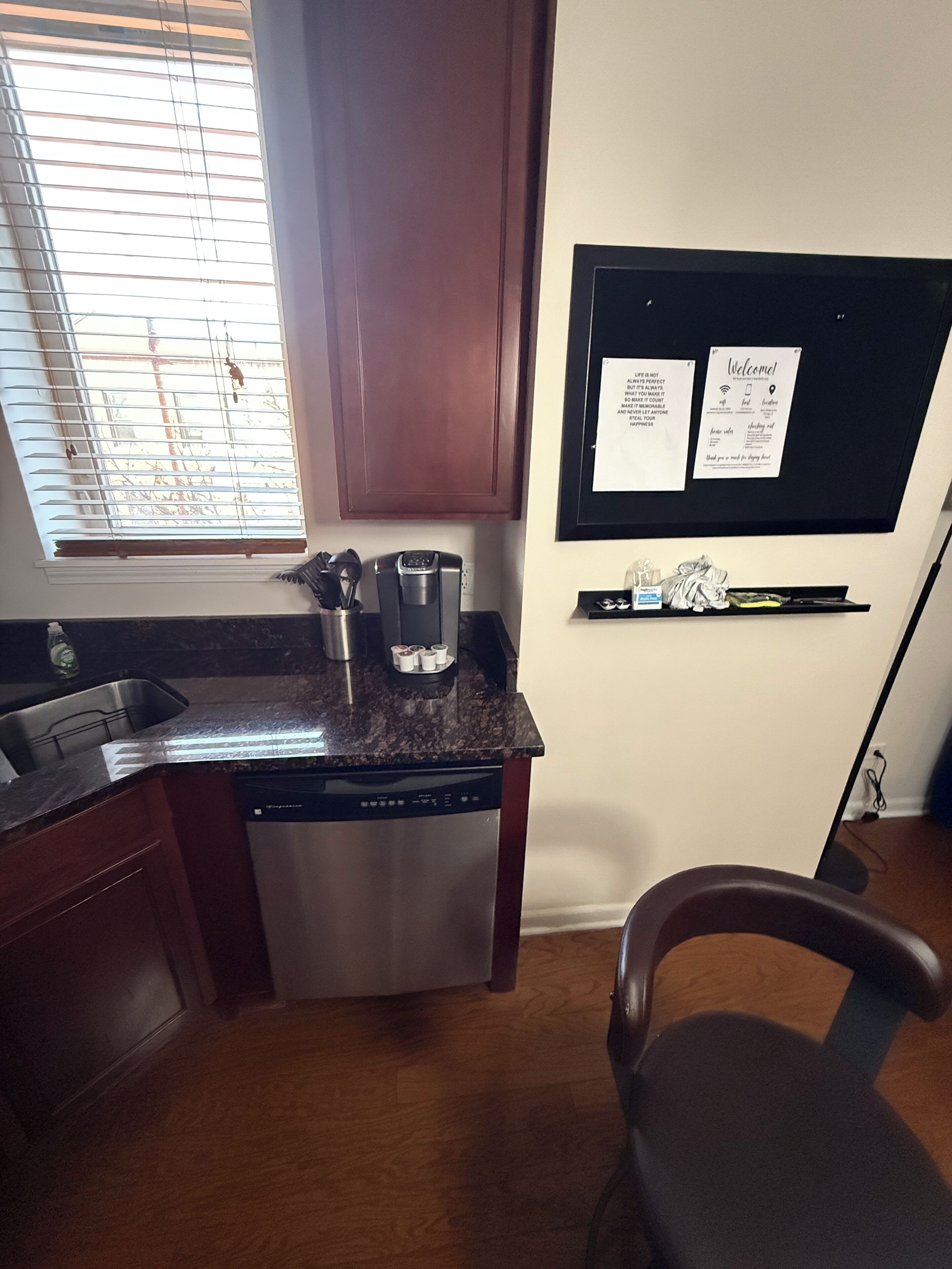 Una cocina con lavavajillas, cafetera y un tablón de anuncios con mensajes de bienvenida.