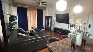 Una sala moderna con un sofá de cuero oscuro, una mesa de comedor de madera con taburetes de bar y un televisor de pantalla plana grande montado en la pared.