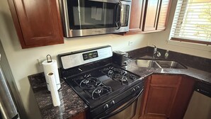 Una cocina con armarios de madera, un microondas de acero inoxidable, una estufa a gas y un lavavajillas.
