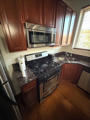 A kitchen with wooden cabinets, a stainless steel microwave, a gas stove, and a dishwasher. - Modern 2BR, Private Elevator, Near United Center and Secure Parking (Chicago)