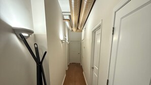 Un pasillo estrecho con suelo de madera, paredes blancas y puertas a ambos lados.