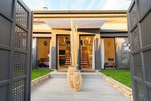 A modern house with a glass door entrance, a staircase leading to the upper floor, and two large decorative vases in the foreground.