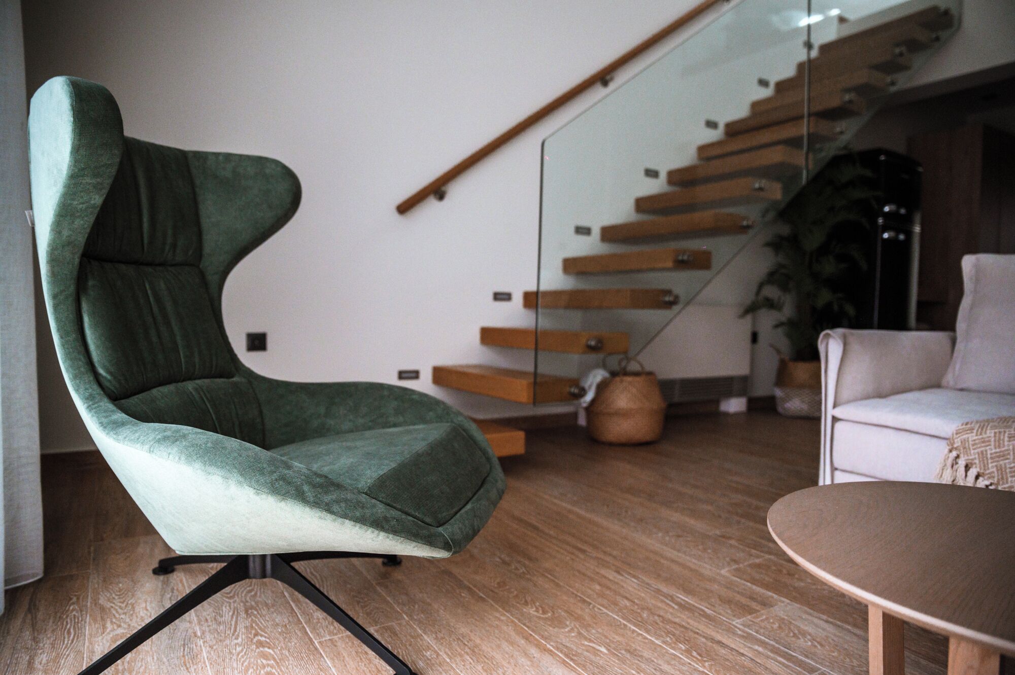 Una sala moderna con un sillón verde, una escalera de madera y un sofá blanco.