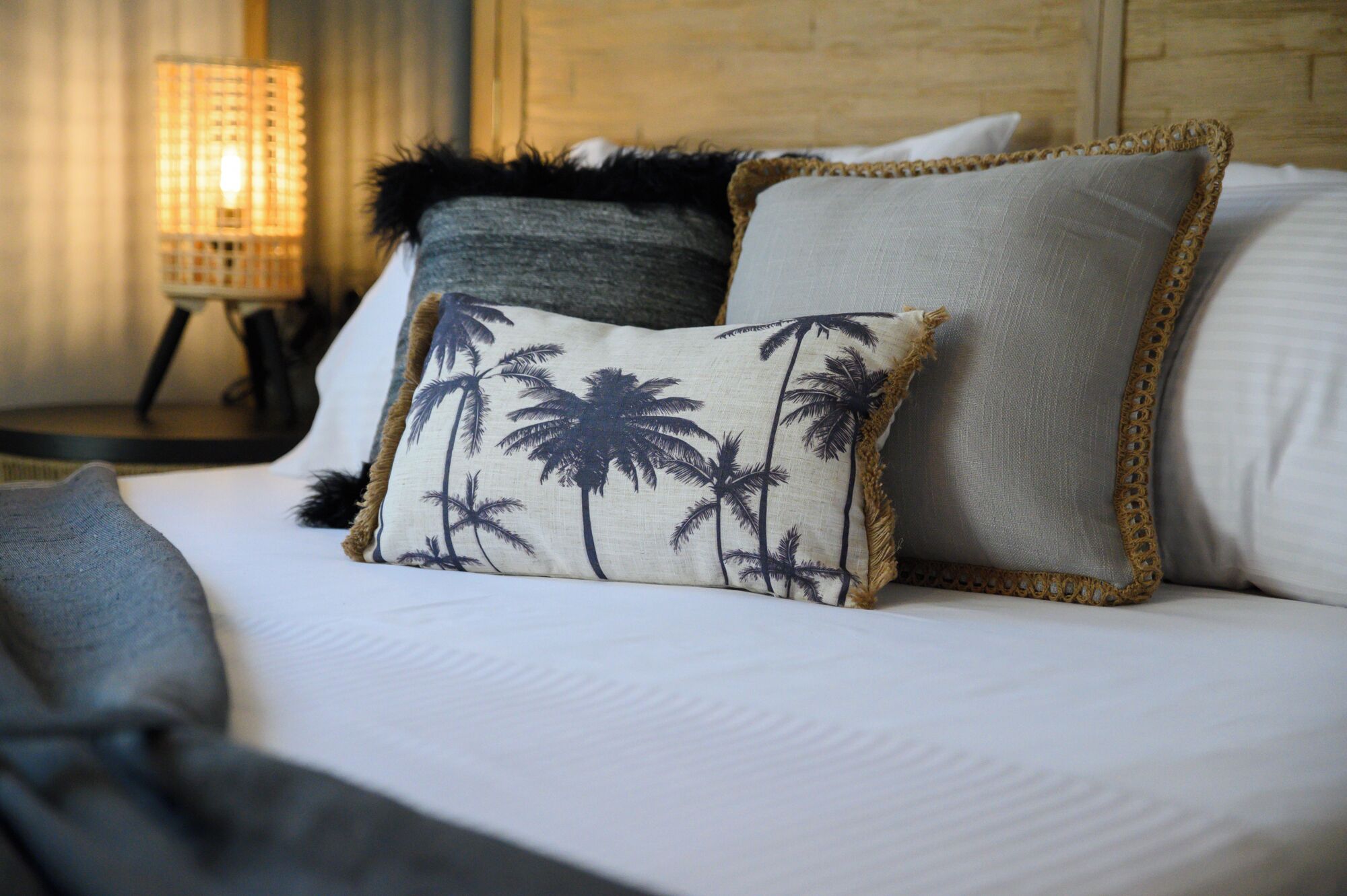 A bed with white bedding, a pillow with a palm tree pattern, and a fluffy pillow.