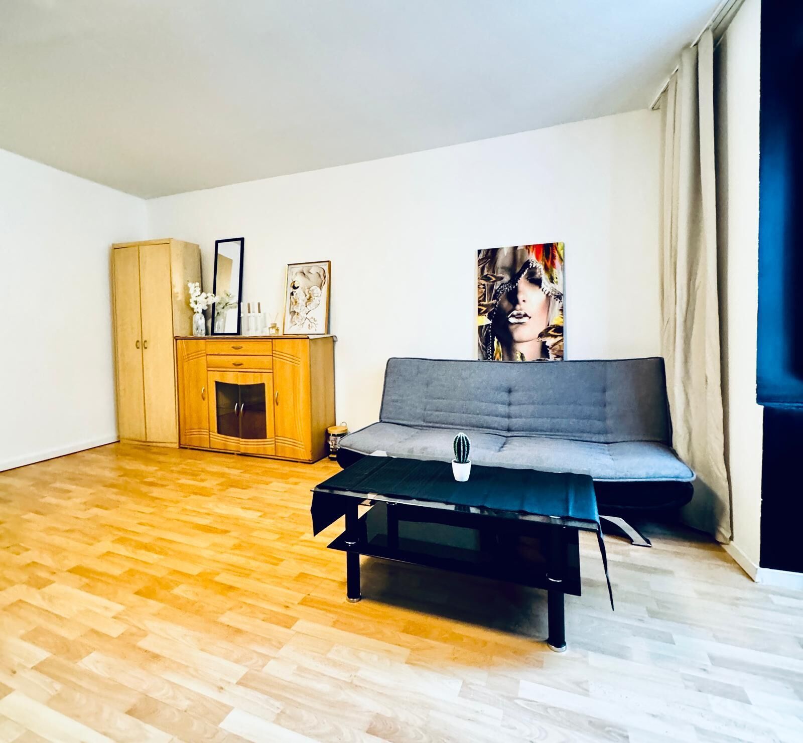 A modern living room with a grey sofa, wooden cabinet, and a painting on the wall.