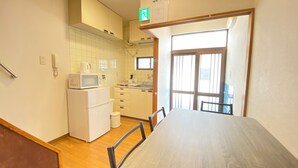 A compact kitchen with a microwave, sink, and cabinets. There is a dining table with chairs and a window providing natural light. - AkiraHome Tsutenkaku West (Osaka)