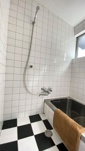 A bathroom with white tiled walls, a black and white checkered floor, a bathtub, and a towel hanging on the side. - AkiraHome Tsutenkaku West (Osaka)