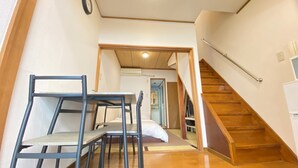 A narrow hallway with a wooden staircase, a bed, and a table with chairs. - AkiraHome Tsutenkaku West (Osaka)