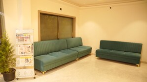 A room with two green sofas, a potted plant, and a whiteboard with notices.
