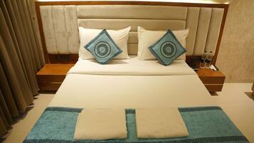 A neatly made bed with a headboard, two pillows, a blue throw blanket, and a bedside table with a remote control and water bottles.