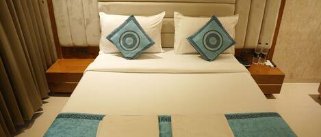 A neatly made bed with a headboard, two pillows, a blue throw blanket, and a bedside table with a remote control and water bottles.