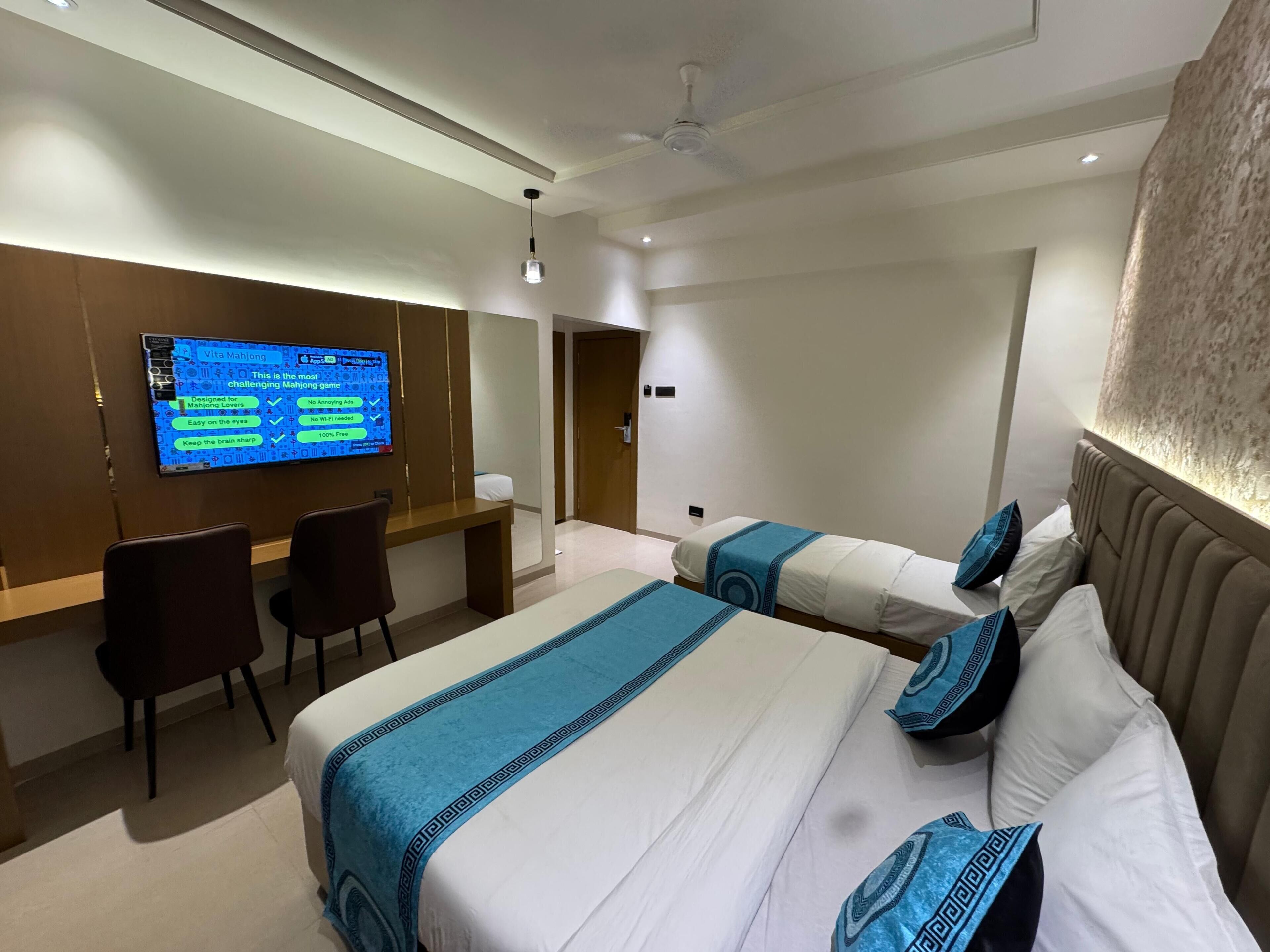 A hotel room with two beds, a desk, a chair, and a TV displaying a game.